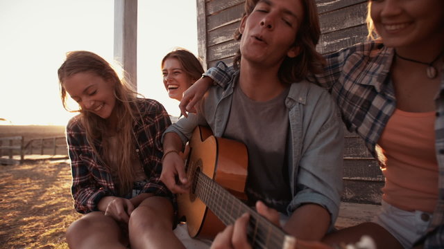 Teen guy playing the guitar for friends on summer afternoon