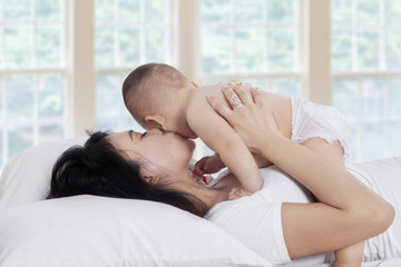 Obraz na płótnie Canvas Happy mother kissing baby on bed