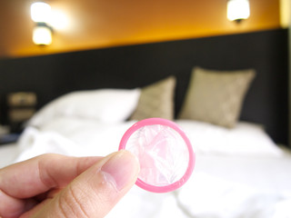 Holding a condom in a hotel with a messy bed