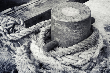 Old rusted mooring bollard with naval ropes