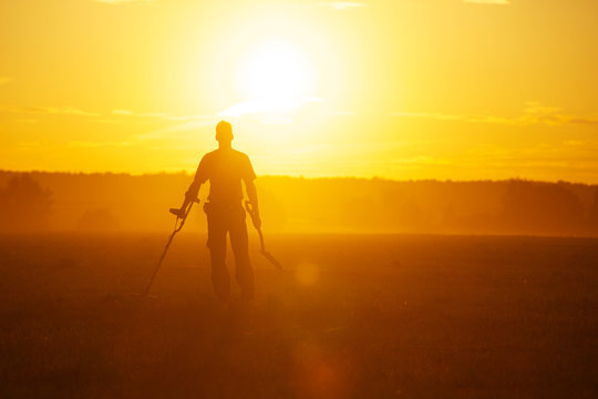 Treasure hunter with Metal detector in the field on the sunset
