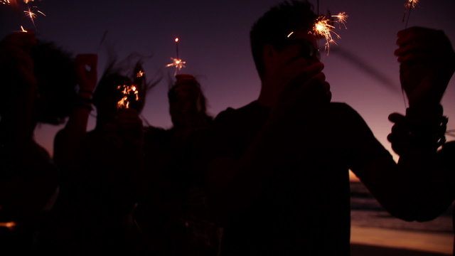 Friends holding sparklers at a beachparty at twilight