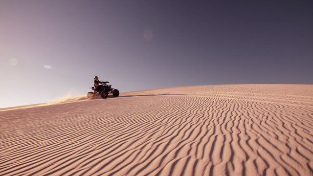 Competitive quad biker kicking up sand while traveling up dune