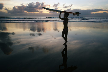 Beautiful young surfer girl in bikini with surfboard on a beach