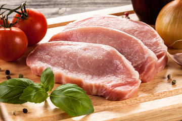 Raw pork chops on cutting board and vegetables