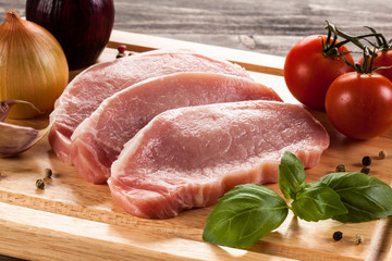 Raw pork chops on cutting board and vegetables