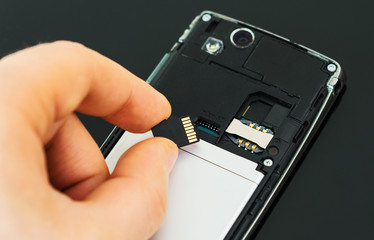 Male hand inserting Micro SD card to mobile phone.