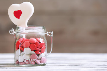 Sweet candies in glass jar with hearts on wooden background