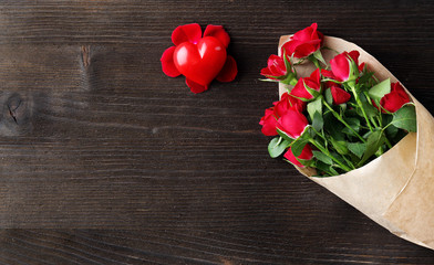Red roses wrapped in paper with heart on wooden table