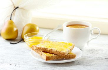Toasts with honey on plate and cup of tea on light background