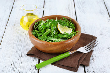 Bowl of green salad and sliced lemon on wooden background