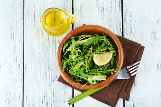 Bowl of green salad and sliced lemon on wooden table, top view