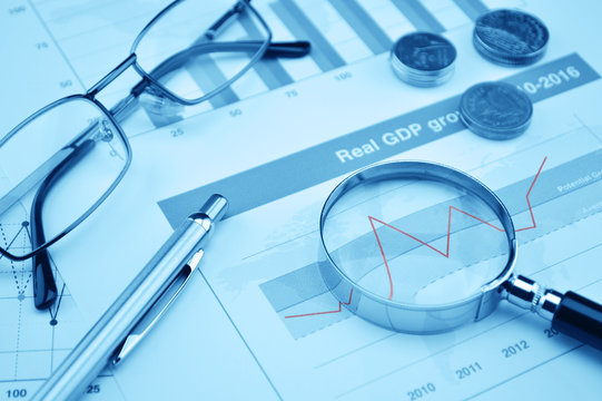 Magnifying glass, pen and glasses on financial chart and graph