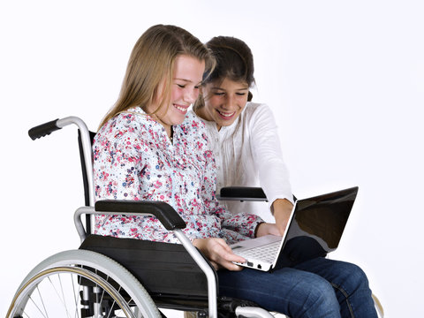 Girl sat in a wheelchair studying with a friend with a computer