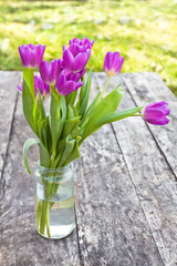 bouquet of violet tulips on the oak brown table in a glass jar