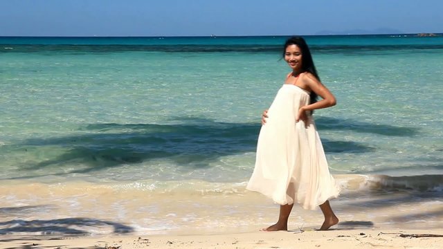 Pregnant woman in white dress walking on the beach