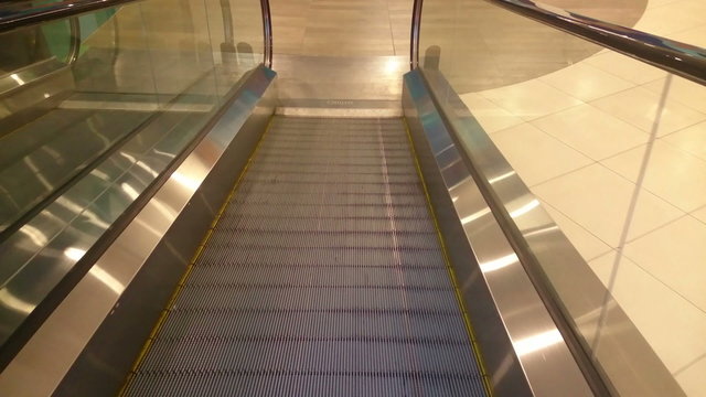 Escalator slowly moving down, reaching end, shopping mall