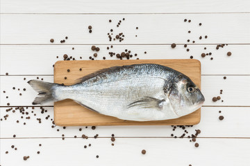 Fresh dorado fish on wooden cutting board with peppercorns