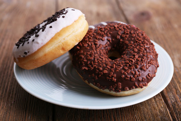 Delicious donuts with icing on plate on wooden background
