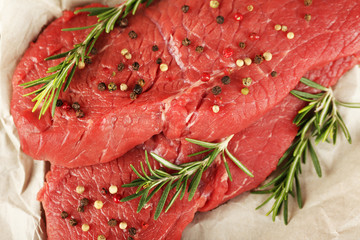 Raw beef steak with rosemary and spices on paper close up