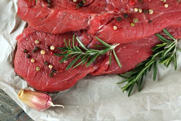 Raw beef steak with rosemary and spices on paper close up