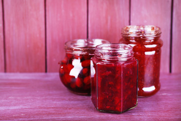 Homemade jars of fruits jam on color wooden background