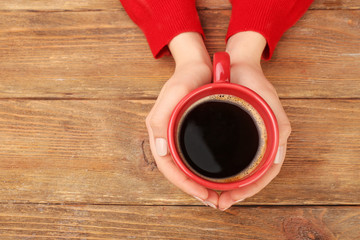 Female hands holding cup of coffee on wooden background
