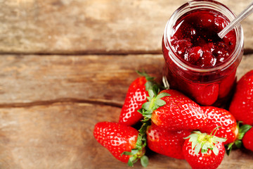 Jar of strawberry jam with berries on wooden background