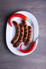 Grilled sausages on plate with chili pepper on table close up