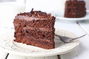 Sliced tasty chocolate cake in plate on wooden table, closeup