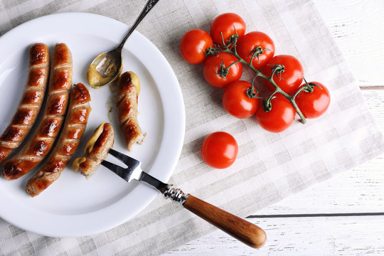 Grilled sausages on plate and cherry tomatoes on table close up