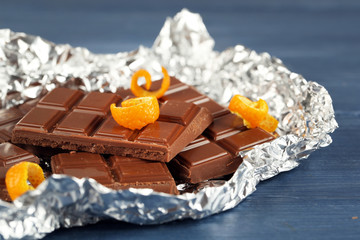 Chocolate with orange peels in foil on wooden table, closeup