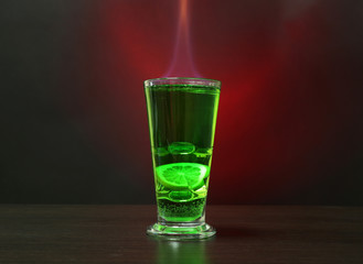 Flaming green cocktail on colorful background