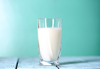 Glass of milk on wooden table on blue background