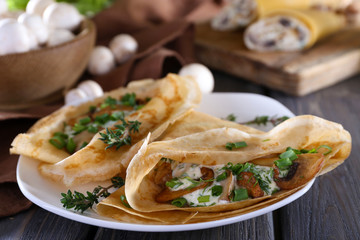 Pancakes with creamy mushrooms in plate on wooden table,
