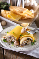 Pancakes with creamy mushrooms in plate on wooden table,