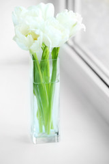 Beautiful white tulips in glass vase on windowsill background