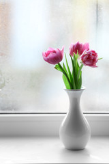 Beautiful pink tulips in vase on windowsill background