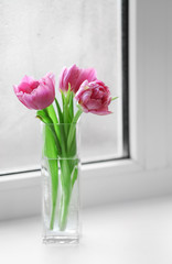 Beautiful pink tulips in vase on windowsill background