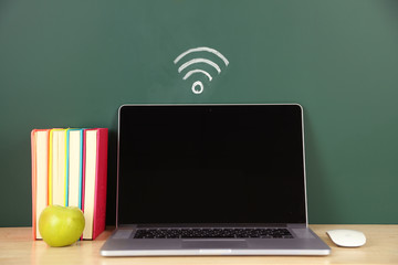 Laptop on table, on green blackboard background