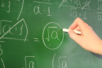 Teacher hand writing formulas on blackboard background