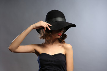 Portrait of beautiful model in black dress and hat on gray background
