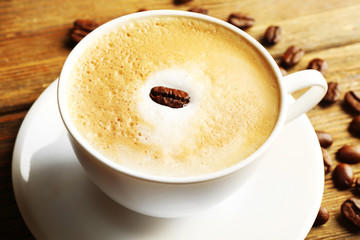 Cup of latte art coffee with grains on wooden table, closeup