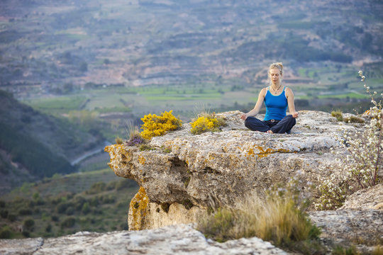 Young woman sitting on a rock in asana position