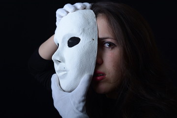 a brunette girl holding a white theatrical mask and cries