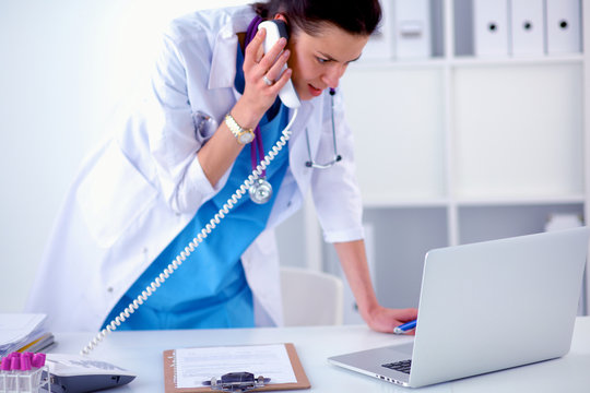 Young Woman Doctor In White Coat At Computer Using Phone