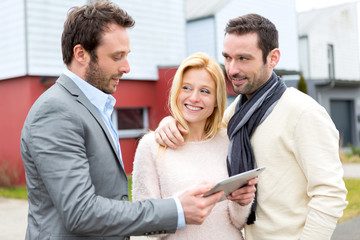 Real estate agent and a young couple in front of their next home