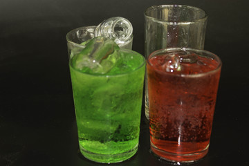Red and green water and ice in a glass on a black background.