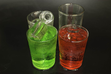 Red and green water and ice in a glass on a black background.