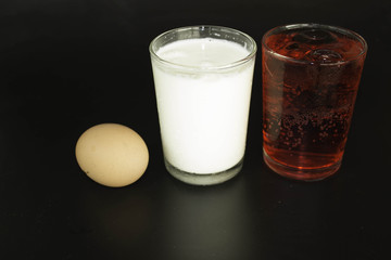 Eggs, milk and water in a glass of red on a black background.